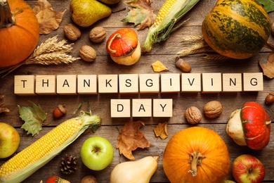 Photo of Cubes with phrase THANKSGIVING DAY, autumn fruits and vegetables on wooden background, flat lay. Happy holiday