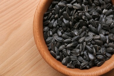 Photo of Organic sunflower seeds in bowl on wooden table, top view. Space for text