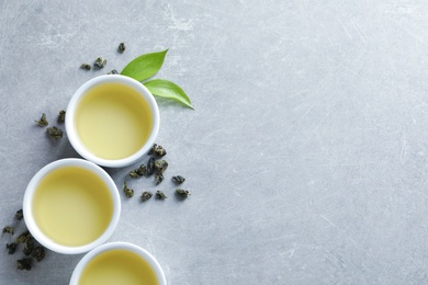 Photo of Cups of Tie Guan Yin oolong and tea leaves on grey background, top view with space for text