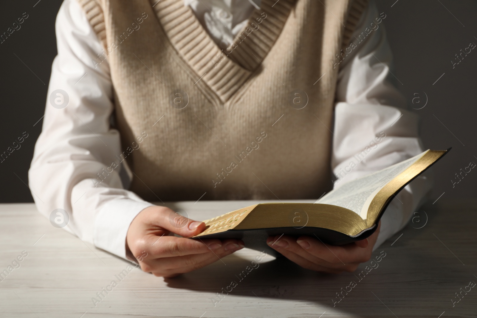 Photo of Woman reading Bible at white wooden table, closeup