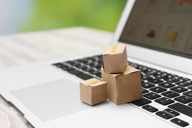 Internet shopping. Small cardboard boxes and laptop on table, closeup. Space for text