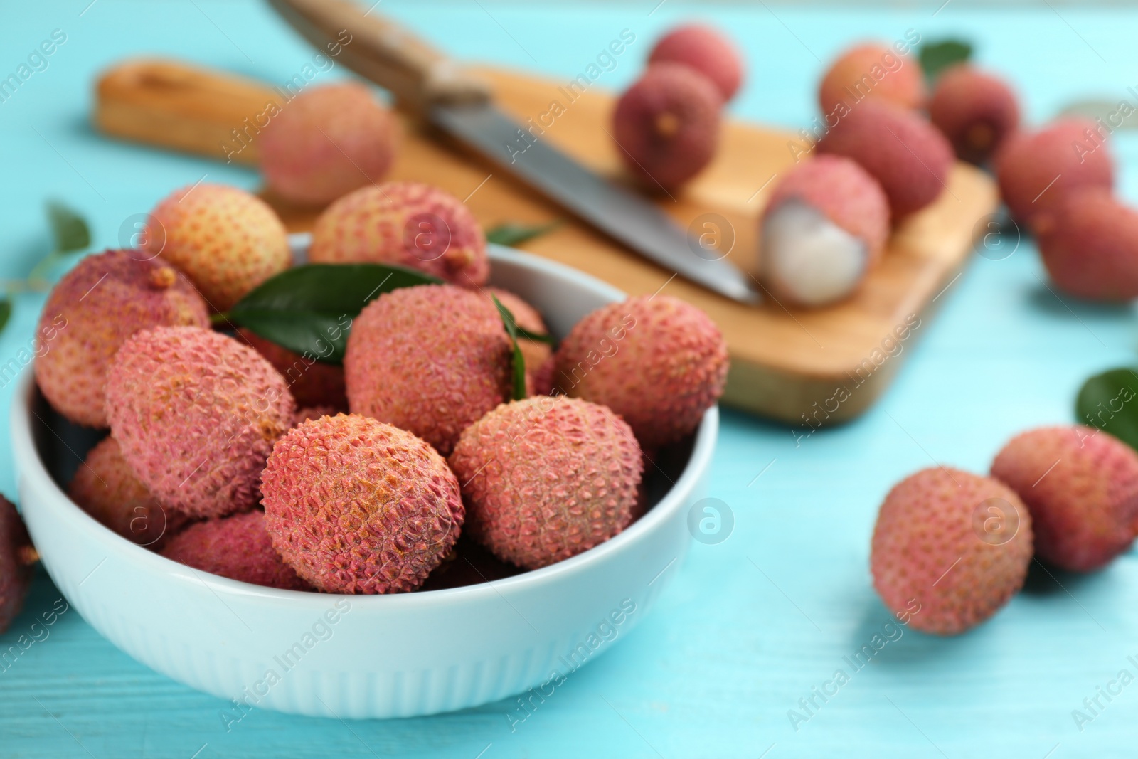 Photo of Fresh ripe lychee fruits in bowl on light blue wooden table. Space for text