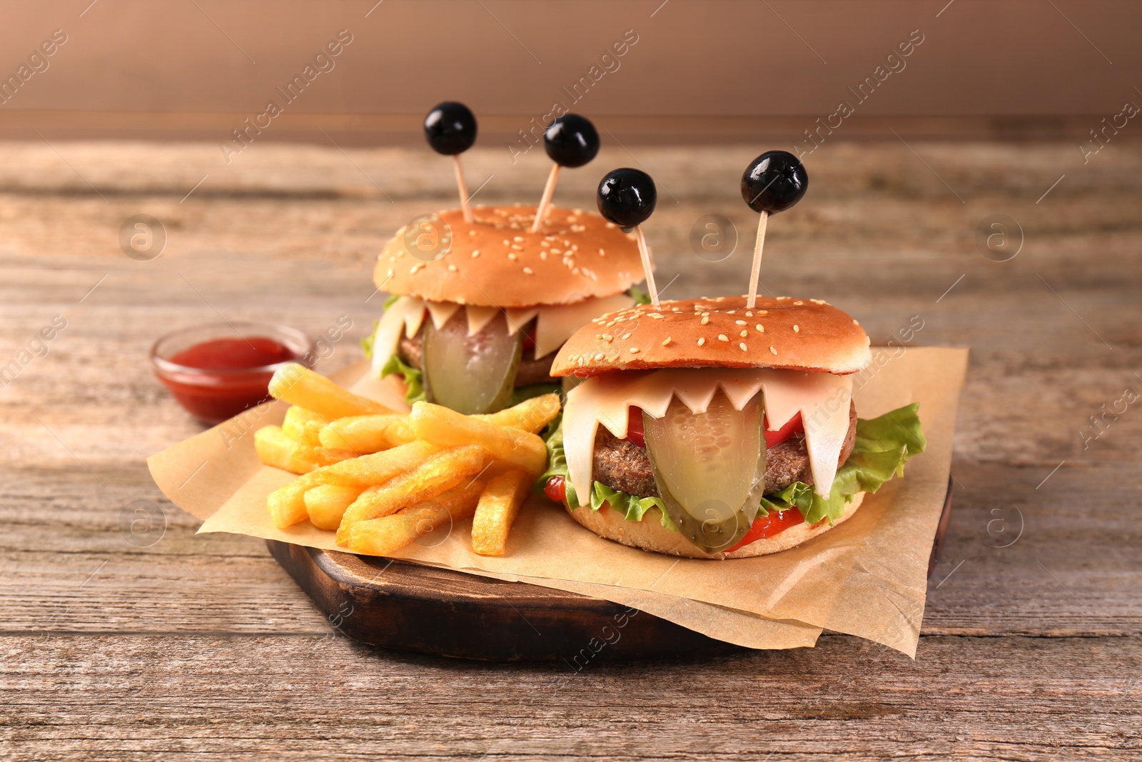 Photo of Cute monster burgers served with french fries and ketchup on wooden table. Halloween party food