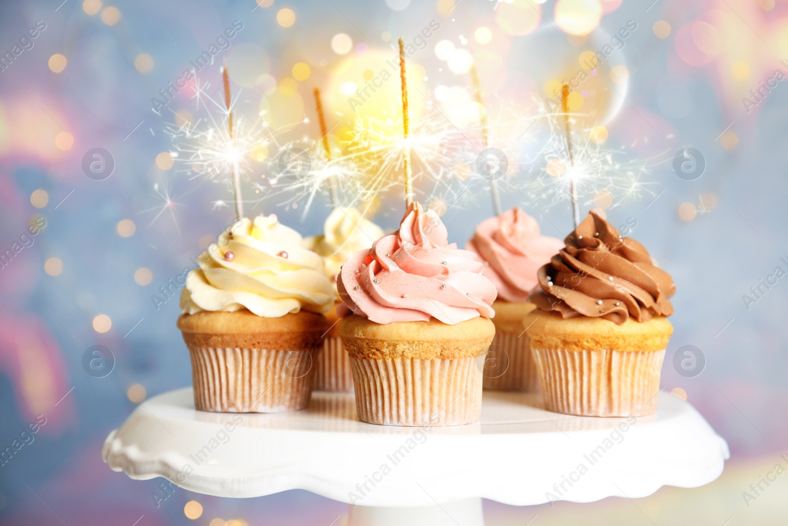 Image of Delicious birthday cupcakes with sparklers on stand against blurred background