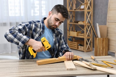 Photo of Young handyman working with electric drill at table in workshop