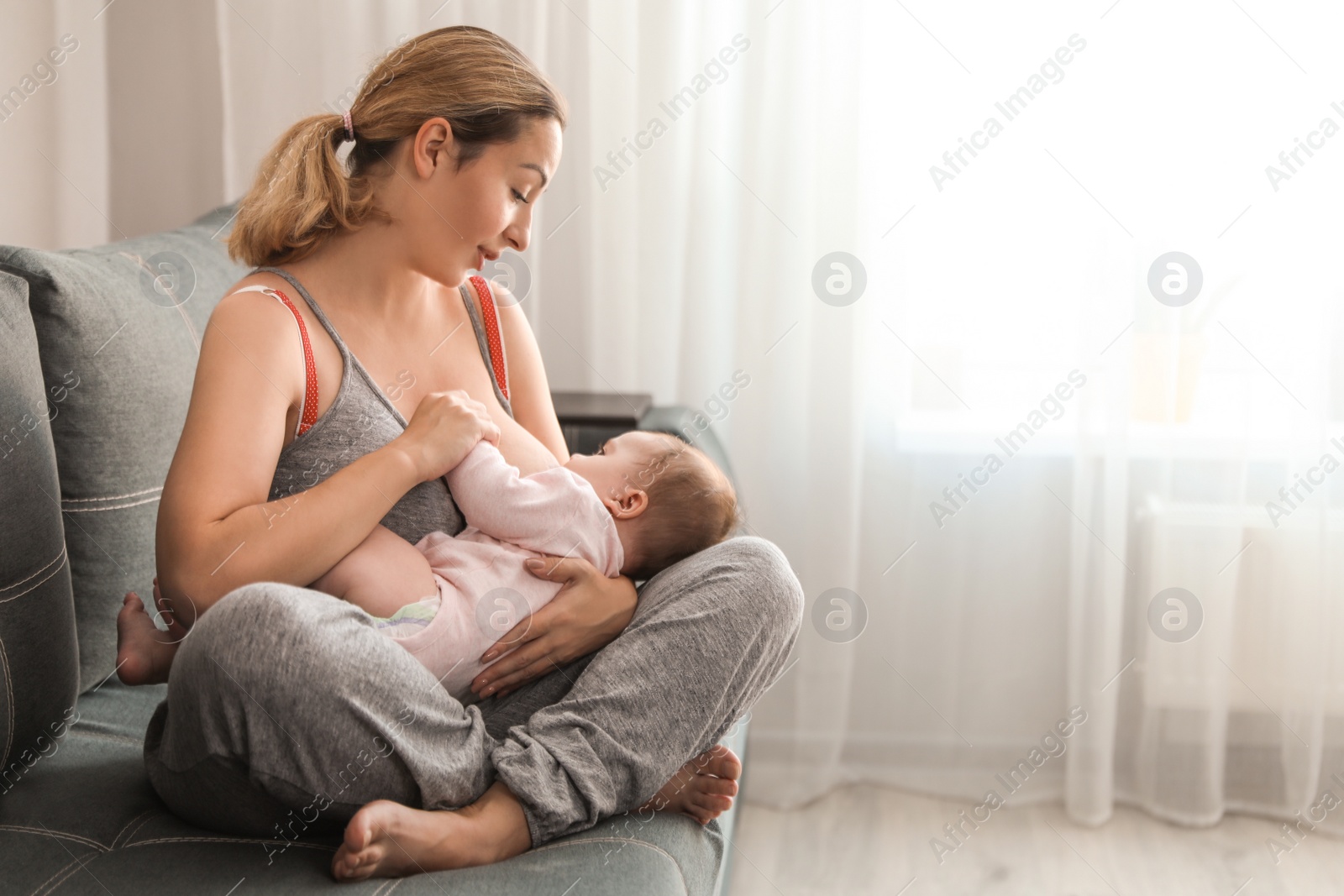 Photo of Young woman breastfeeding her baby at home. Space for text