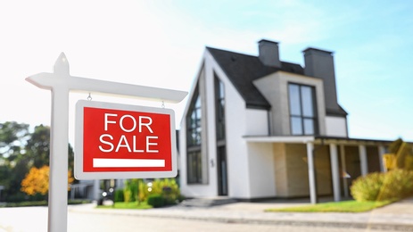 Photo of Red real estate sign near house outdoors on sunny day