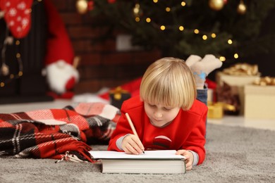 Photo of Little child writing letter to Santa Claus on floor at home. Christmas celebration