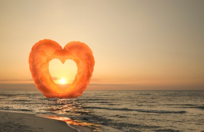 Image of Picturesque sunset at sea. Sun going down, view through gap in heart formed from clouds