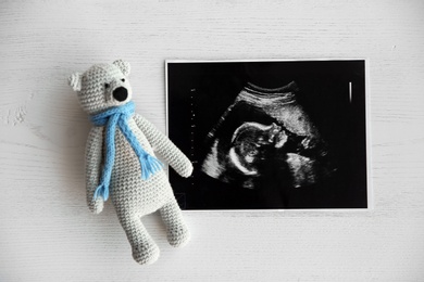 Ultrasound photo of baby and toy on wooden background, top view