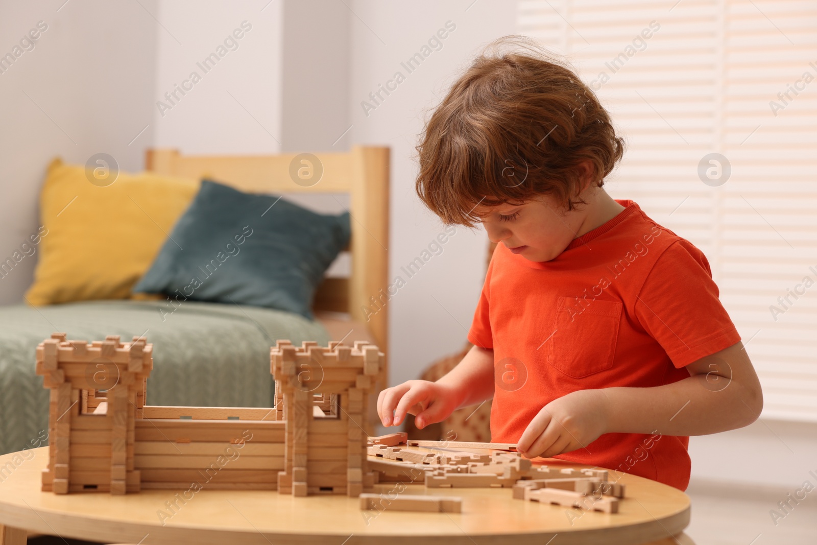 Photo of Cute little boy playing with wooden construction set at table in room. Child's toy