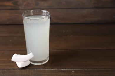 Glass of coconut water and nut on wooden table, space for text