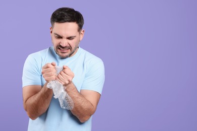 Photo of Emotional man with bubble wrap on purple background. Space for text