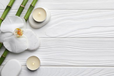 Photo of Bamboo stems, orchid, spa stones and burning candles on white wooden table, flat lay. Space for text