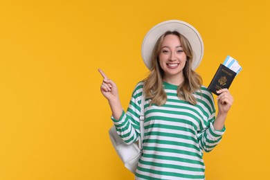 Photo of Happy young woman with passport, ticket and hat pointing at something on yellow background, space for text