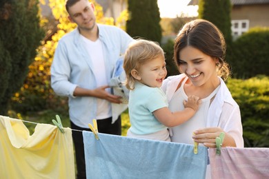 Photo of Happy family hanging clothes with clothespins on washing line for drying in backyard