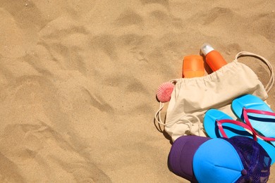 Sunscreens, seashell and beach accessories on sand, flat lay. Space for text