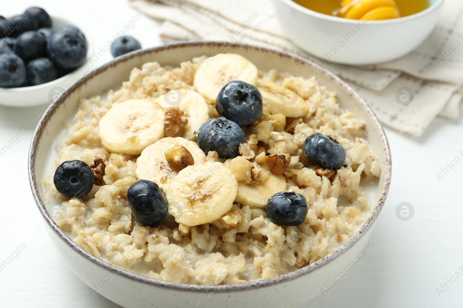 Photo of Tasty oatmeal with banana, blueberries, walnuts and honey served in bowl on white wooden table, closeup