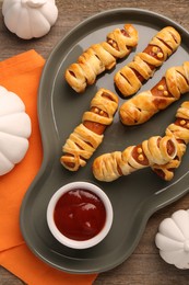 Cute sausage mummies served with ketchup on wooden table, flat lay. Halloween party food