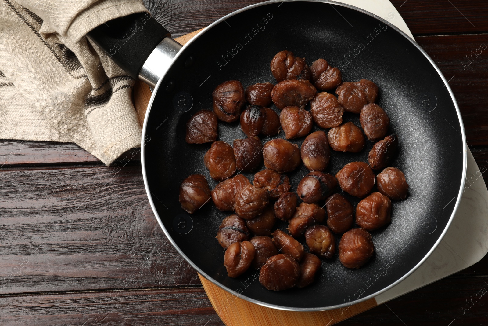 Photo of Roasted edible sweet chestnuts in frying pan on wooden table, top view