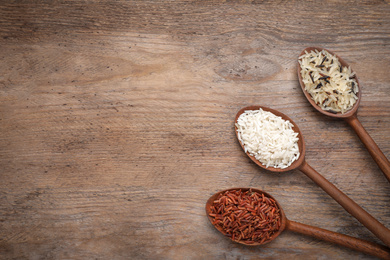 Photo of Brown and polished rice in spoons on wooden table, flat lay. Space for text