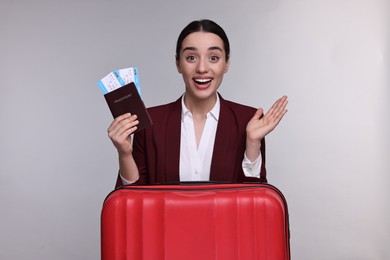 Excited businesswoman with passport, tickets and suitcase on grey background