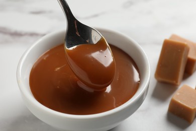 Taking yummy salted caramel with spoon from bowl on table, closeup