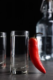 Photo of Red hot chili pepper and vodka on grey table against black background