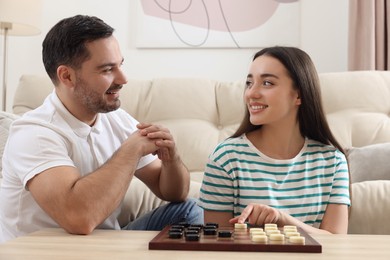 Happy couple playing checkers at table in room