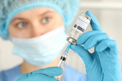 Doctor filling syringe with coronavirus vaccine in laboratory, focus on hands