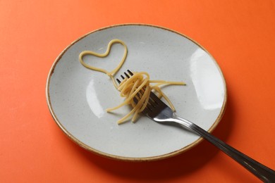 Photo of Heart made of tasty spaghetti and fork on orange background
