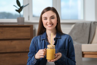Photo of Beautiful young woman with delicious smoothie at home