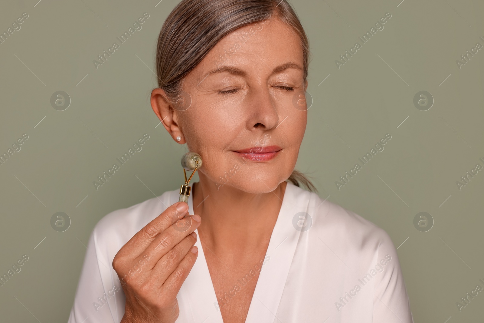 Photo of Woman massaging her face with jade roller on green background