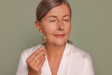 Photo of Woman massaging her face with jade roller on green background