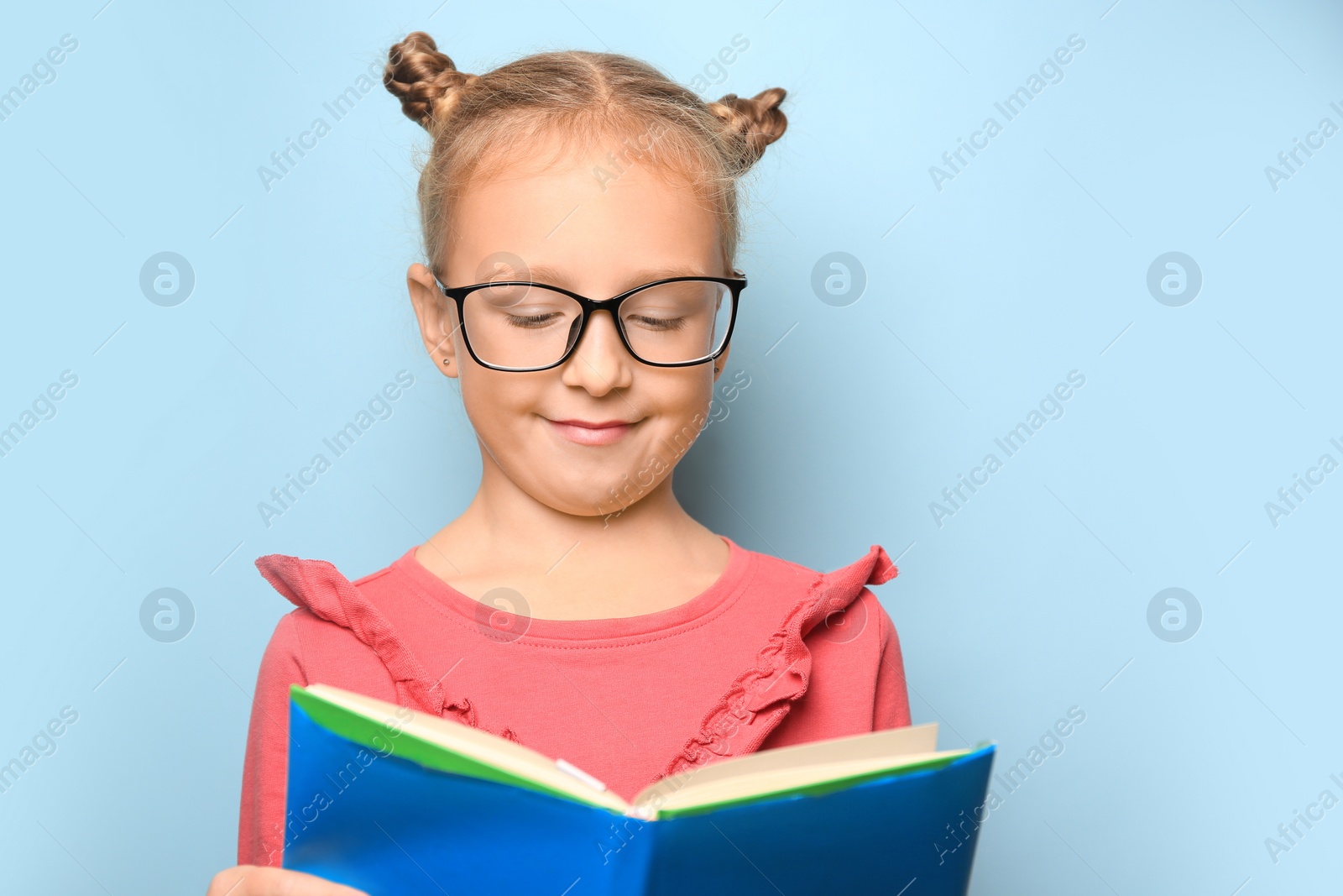 Photo of Cute little girl in glasses reading textbook on light blue background. Space for text