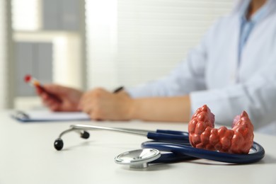 Photo of Endocrinologist working in hospital, focus on thyroid gland model and stethoscope on white table