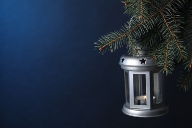 Photo of Christmas lantern with burning candle on fir tree against blue background, closeup. Space for text
