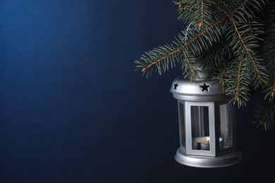 Christmas lantern with burning candle on fir tree against blue background, closeup. Space for text