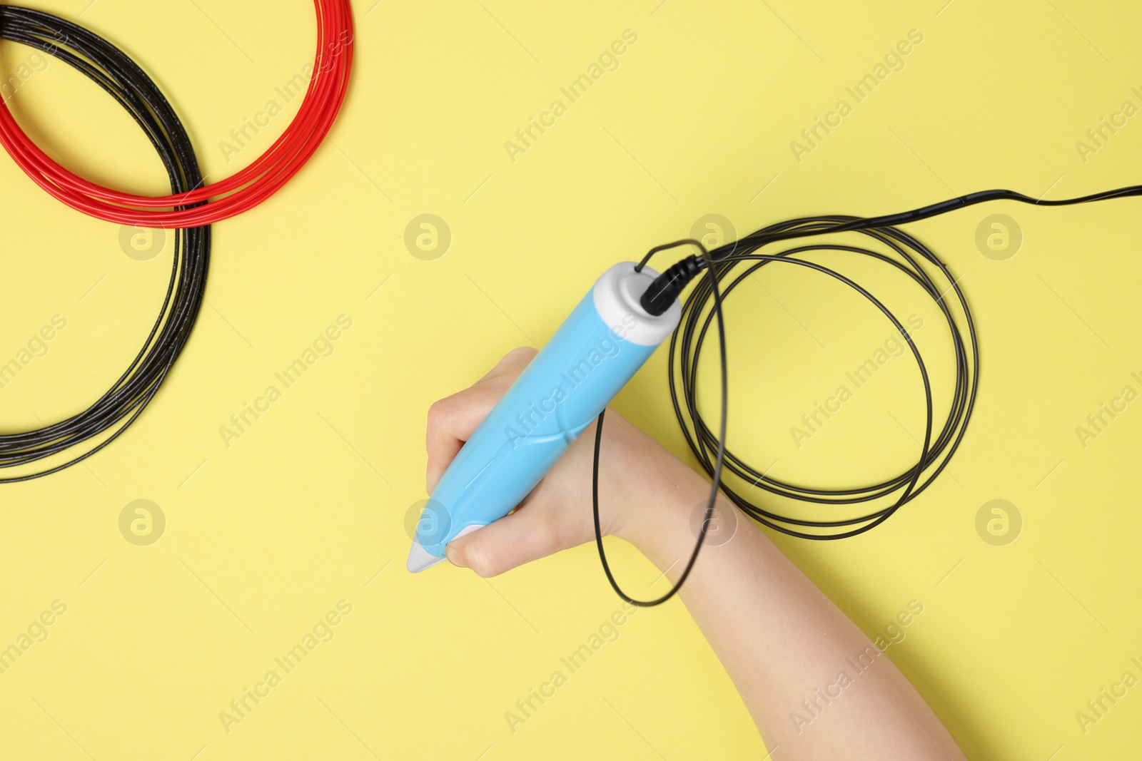 Photo of Boy drawing with stylish 3D pen on yellow background, top view