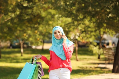 Muslim woman with shopping bags talking on phone in park