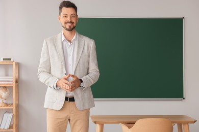 Photo of Happy teacher standing in classroom. Space for text