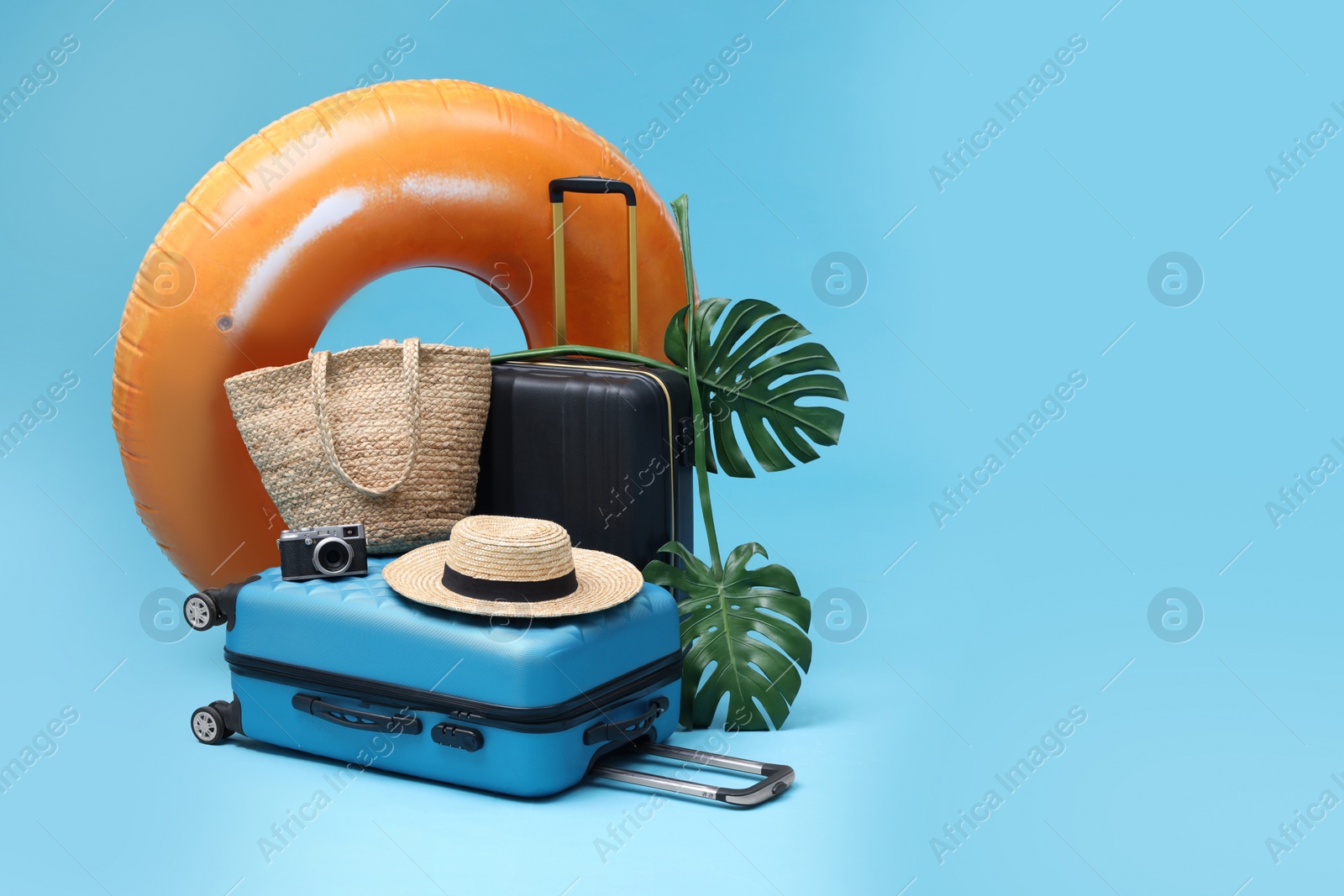 Photo of Suitcases, beach accessories and tropical leaves on light blue background, space for text. Summer vacation