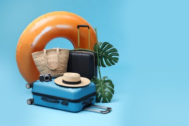 Photo of Suitcases, beach accessories and tropical leaves on light blue background, space for text. Summer vacation