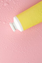 Photo of Moisturizing cream in tube on pink background with water drops, top view. Space for text