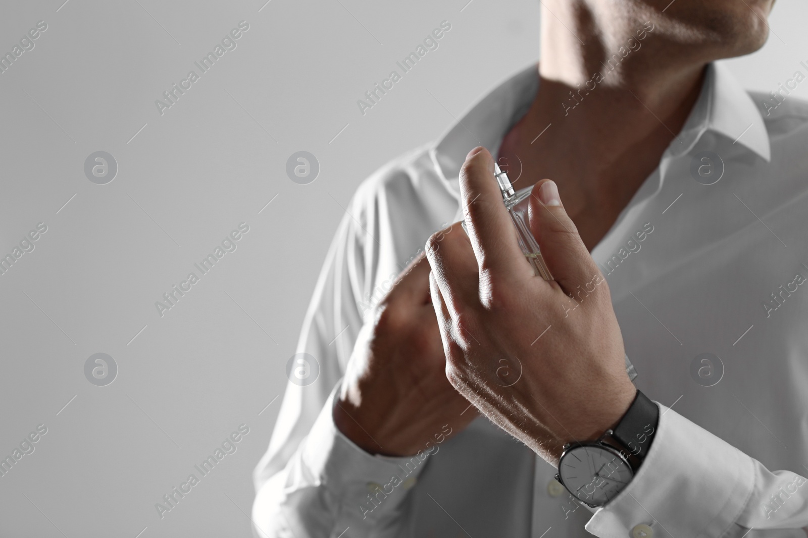 Photo of Handsome man applying perfume on neck against light background, closeup. Space for text