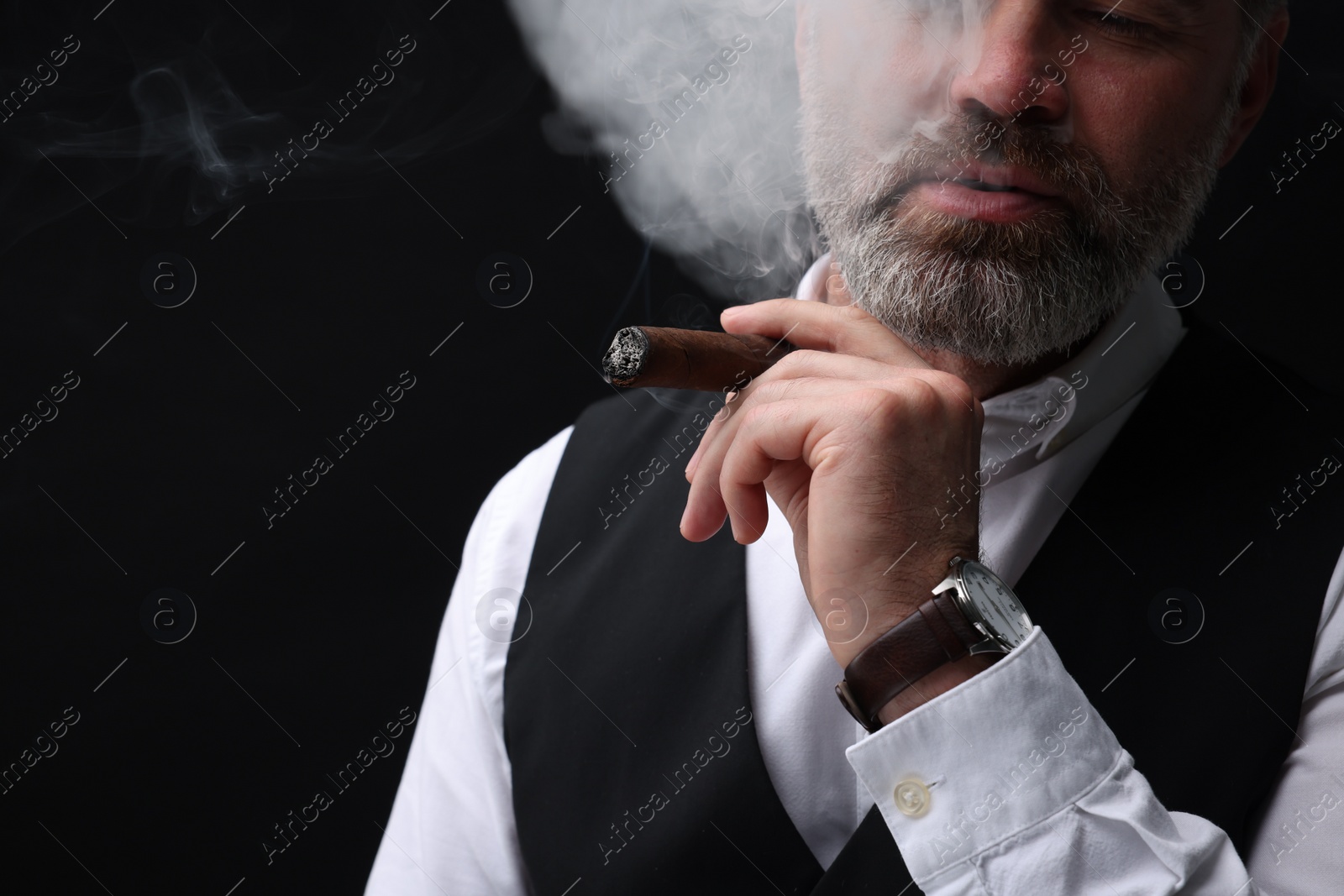 Photo of Bearded man smoking cigar against black background, closeup. Space for text