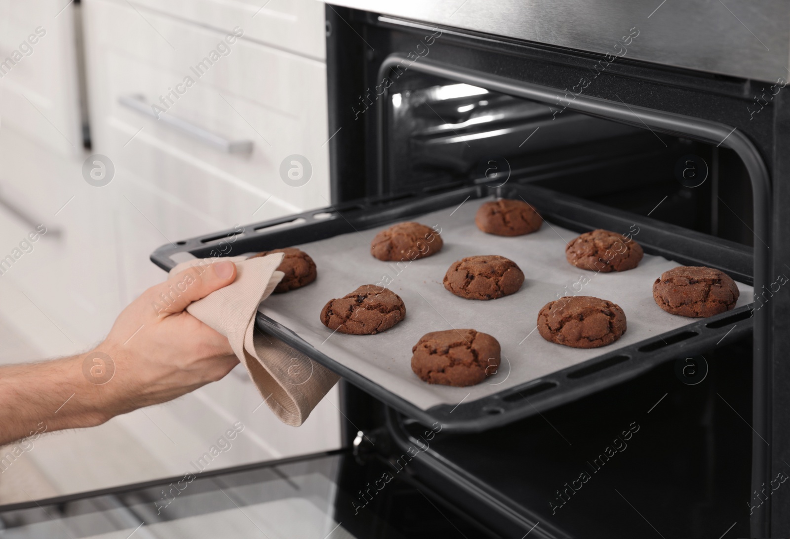 Photo of Man taking out tray of baked cookies from oven in kitchen, closeup