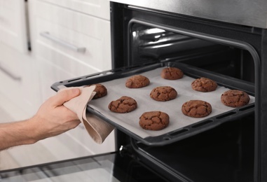 Photo of Man taking out tray of baked cookies from oven in kitchen, closeup