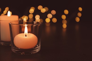 Burning candles in glass holders on table against blurred lights, space for text