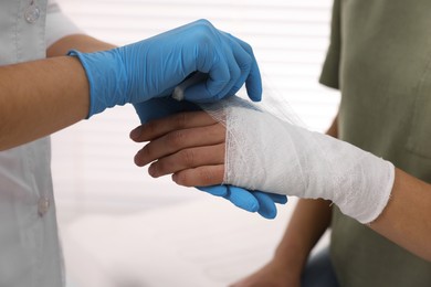 Doctor bandaging patient's burned hand indoors, closeup